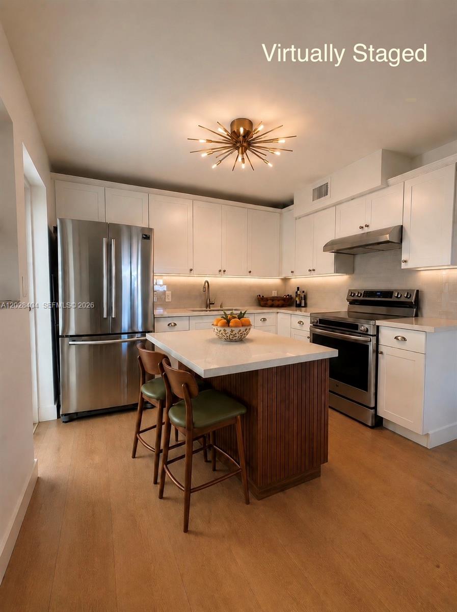 A kitchen features white cabinets, stainless steel appliances, a wood-paneled island, and light wood flooring — 1400 Lincoln Rd # 301, Miami Beach FL 33139, MIAMI BEACH, FL