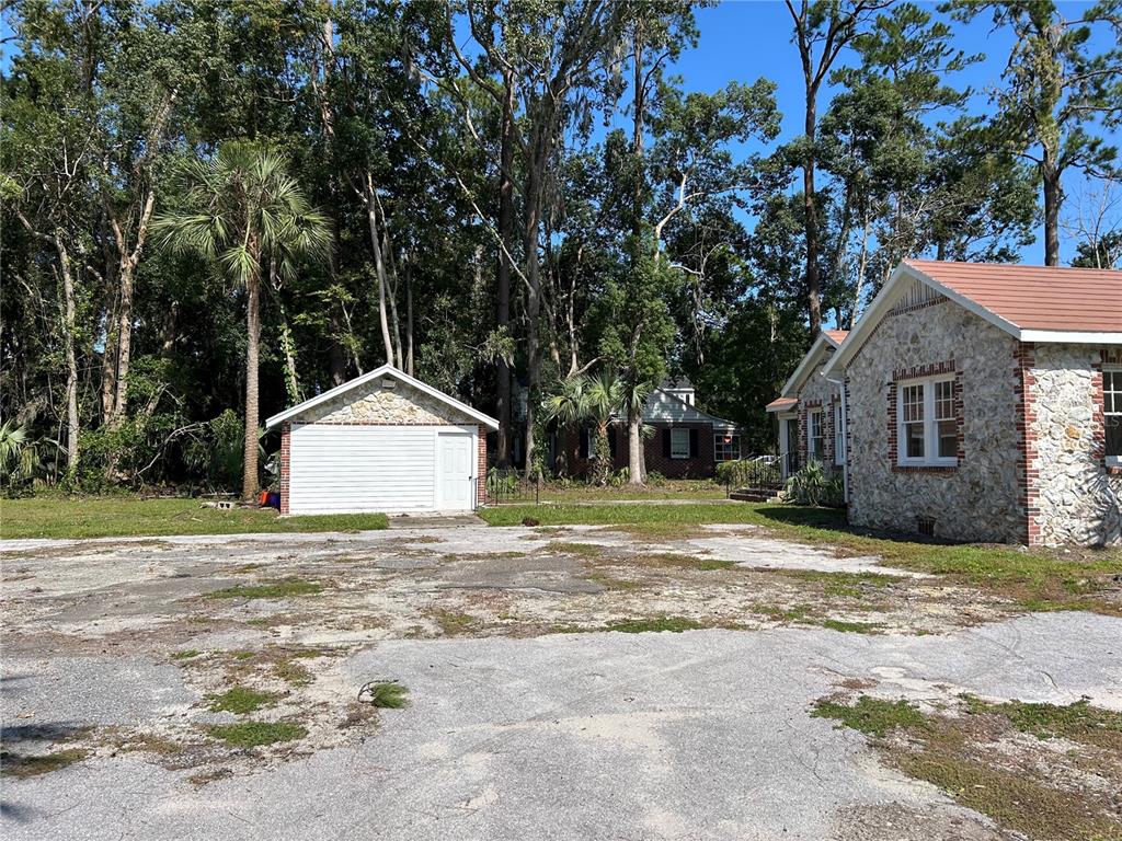 A stone-faced house and detached garage sit on a large, weathered asphalt lot — 1008 NW 13TH STREET, GAINESVILLE, FL