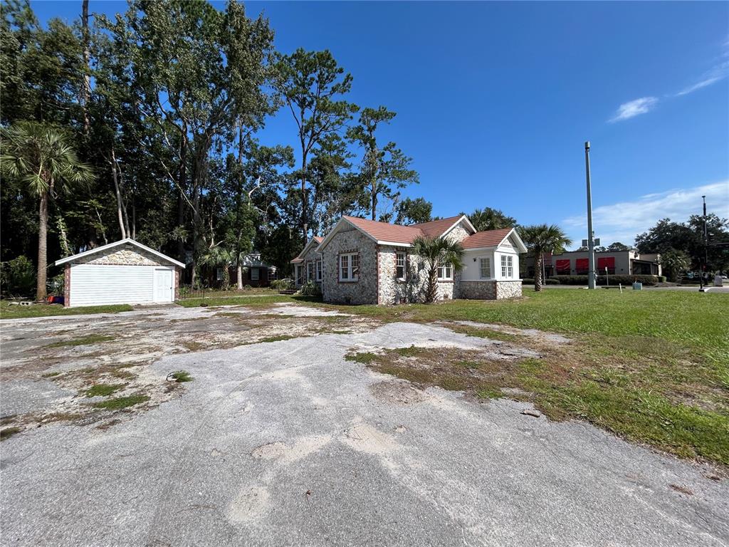 A stone-clad house with a detached garage sits on a large, weathered asphalt lot — 1008 NW 13TH STREET, GAINESVILLE, FL
