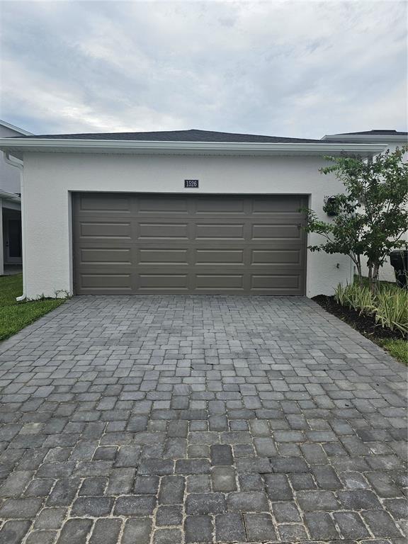 A white house exterior features a brown two-car garage door and a gray paver driveway — 1526 RIDGEBACK LANE, APOPKA, FL