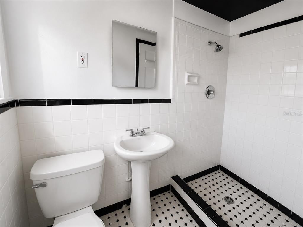 A bathroom features a pedestal sink, toilet, and walk-in shower with white and black tiles — 8010 SE US HIGHWAY 301 UNIT 4A, HAWTHORNE, FL