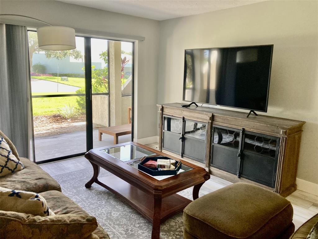A living room features a television on a wooden console, a coffee table, and sliding doors — 6114 43RD STREET W UNIT 103E, BRADENTON, FL