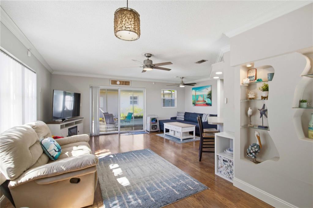 A living room features wood-look flooring, a beige recliner, a blue sofa, and built-in shelving — 6116 DARTMOUTH DRIVE, BRADENTON, FL