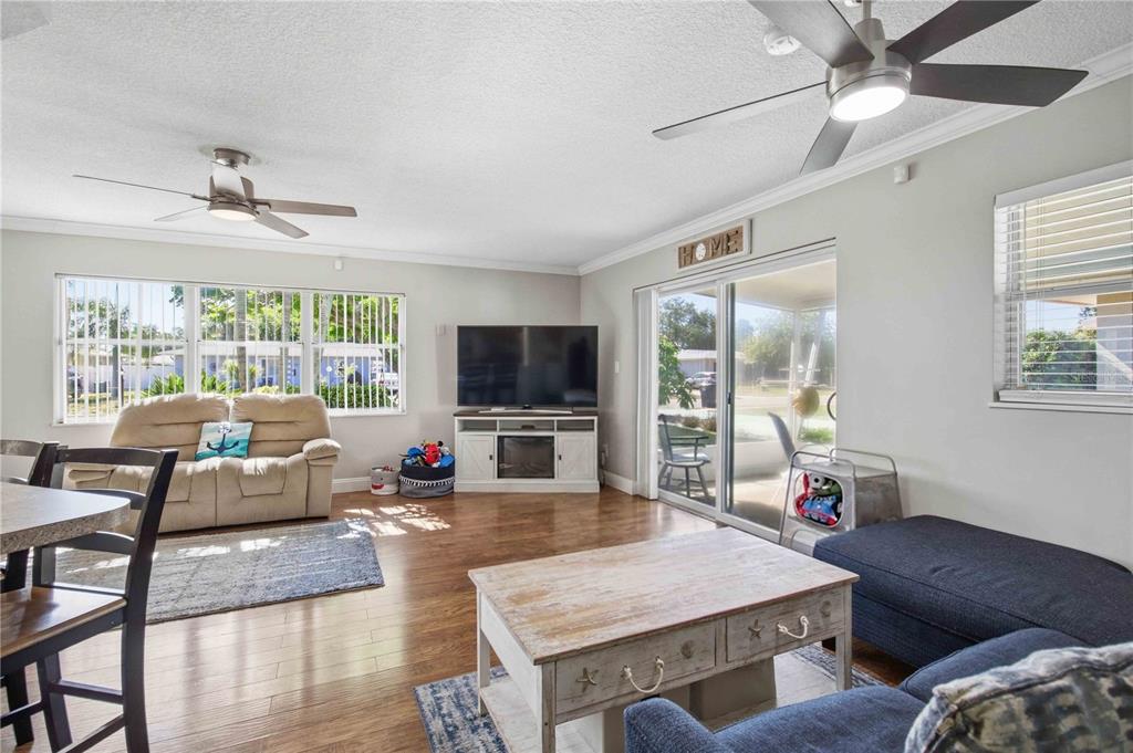 A living room with wood-look flooring, a ceiling fan, a television, and a sliding glass door — 6116 DARTMOUTH DRIVE, BRADENTON, FL