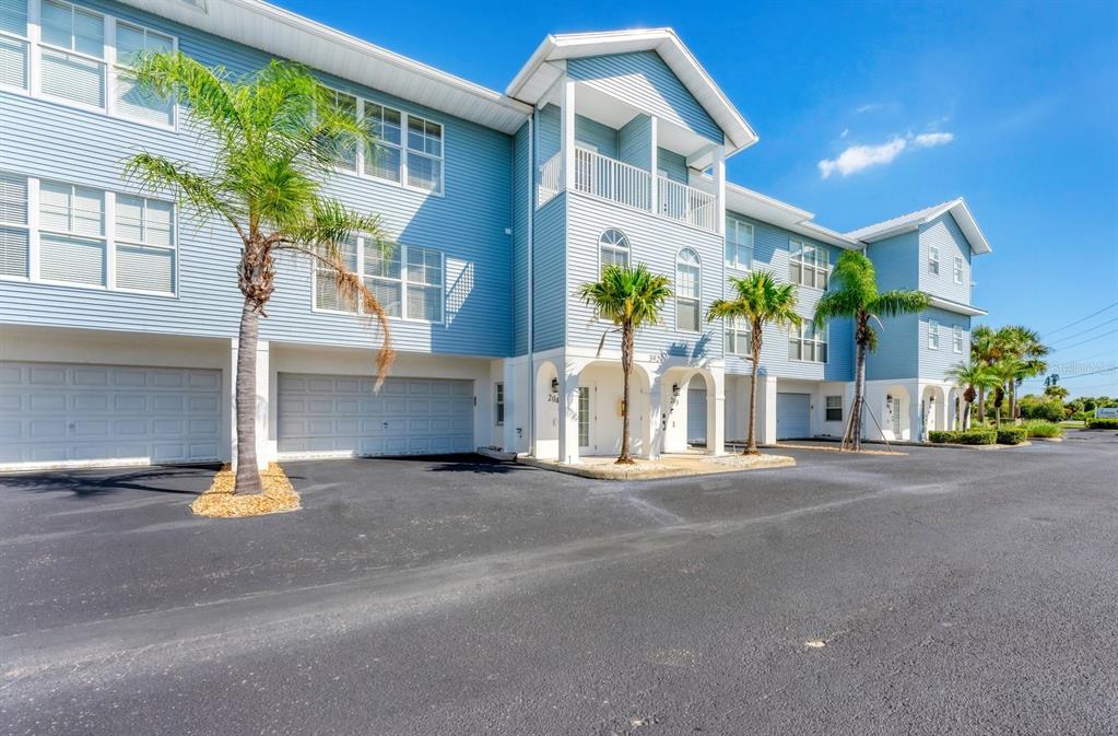 A three-story blue building with a parking garage and palm trees under a clear sky — 3927 CAPE HAZE DRIVE UNIT 204, ROTONDA WEST, FL