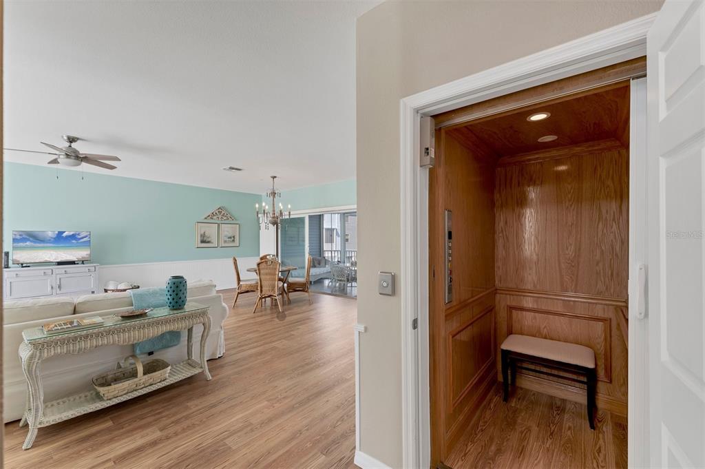 A residential elevator with wood paneling opens into a living room with light blue walls — 3927 CAPE HAZE DRIVE UNIT 204, ROTONDA WEST, FL
