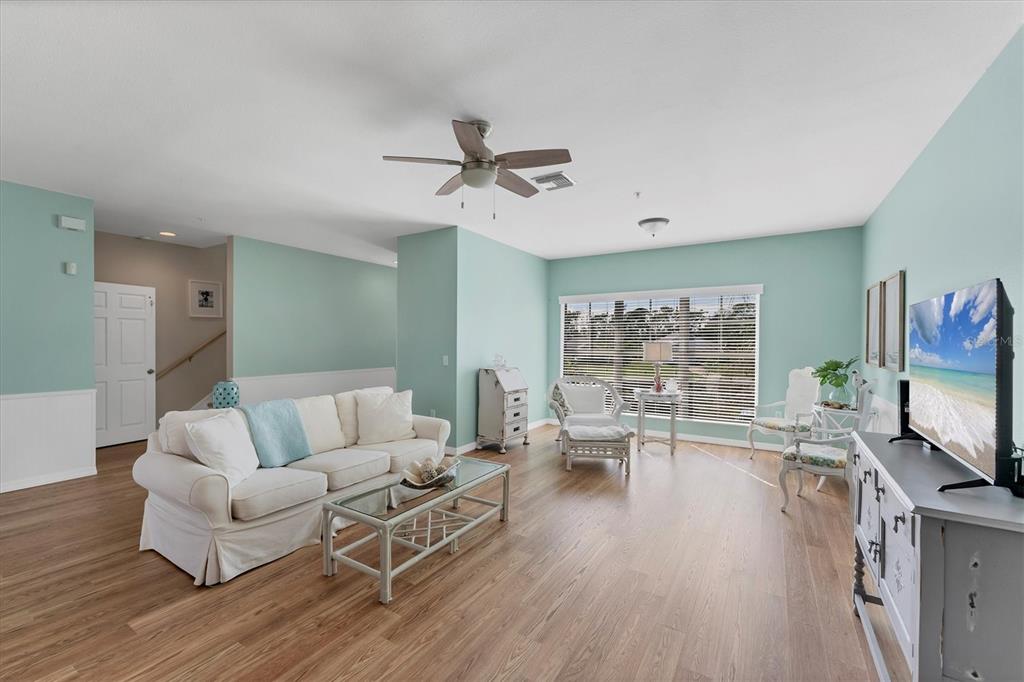 A living room with light blue walls, wood-look flooring, a white sofa, and a television — 3927 CAPE HAZE DRIVE UNIT 204, ROTONDA WEST, FL