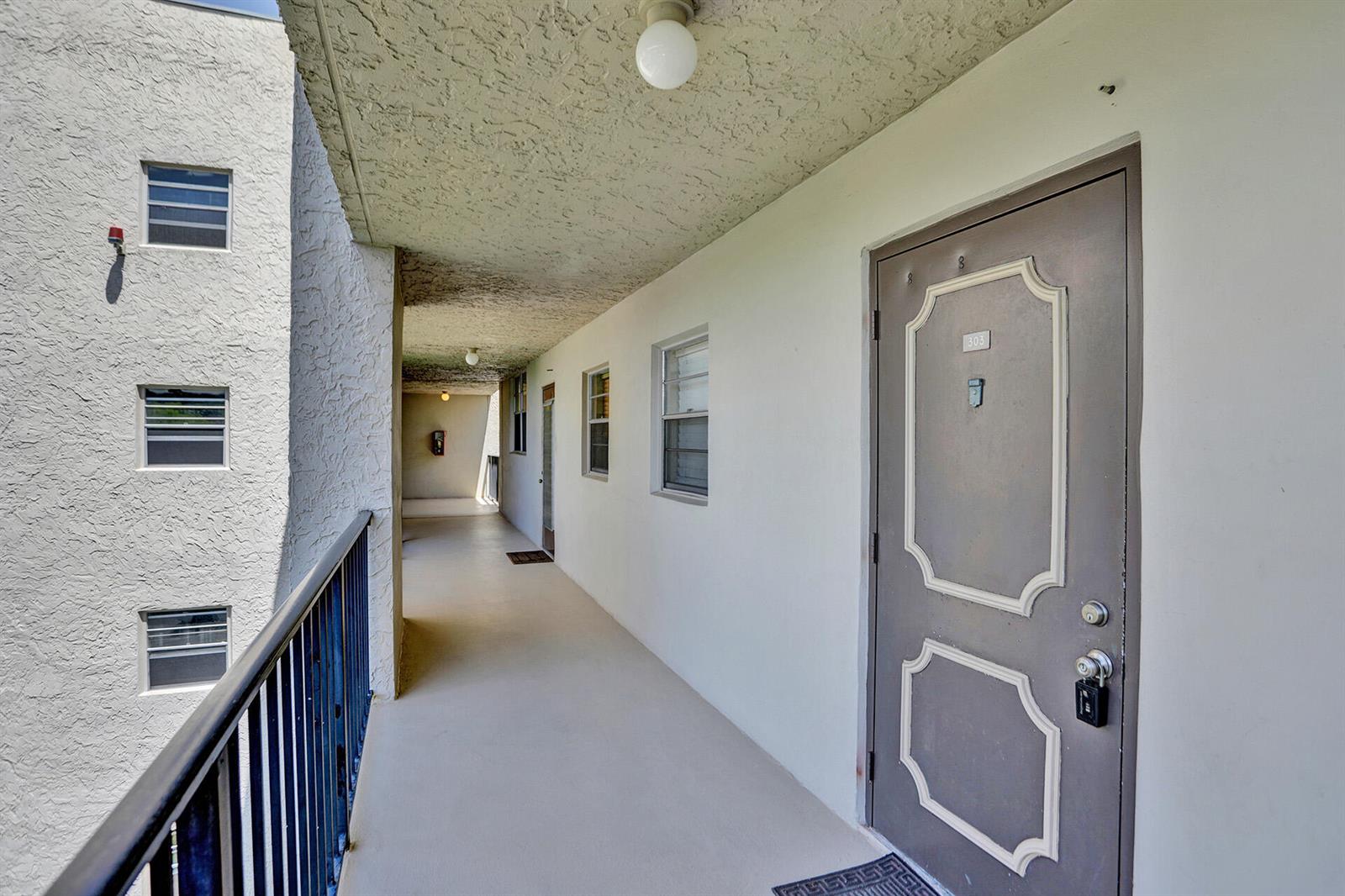 An outdoor apartment building walkway with a brown door labeled 303 and metal railings — 9230 Lagoon Place # 110, Davie FL 33324, DAVIE, FL