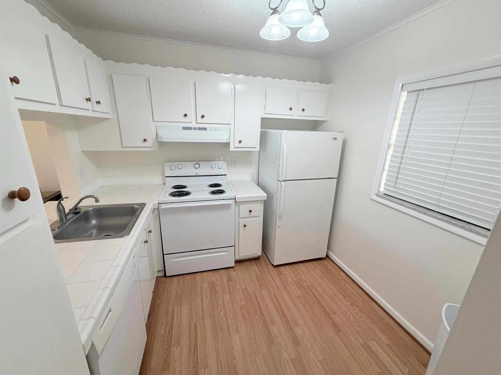 A small kitchen features white cabinets, white appliances, tiled countertops, and light wood-look flooring — 9230 Lagoon Place # 110, Davie FL 33324, DAVIE, FL