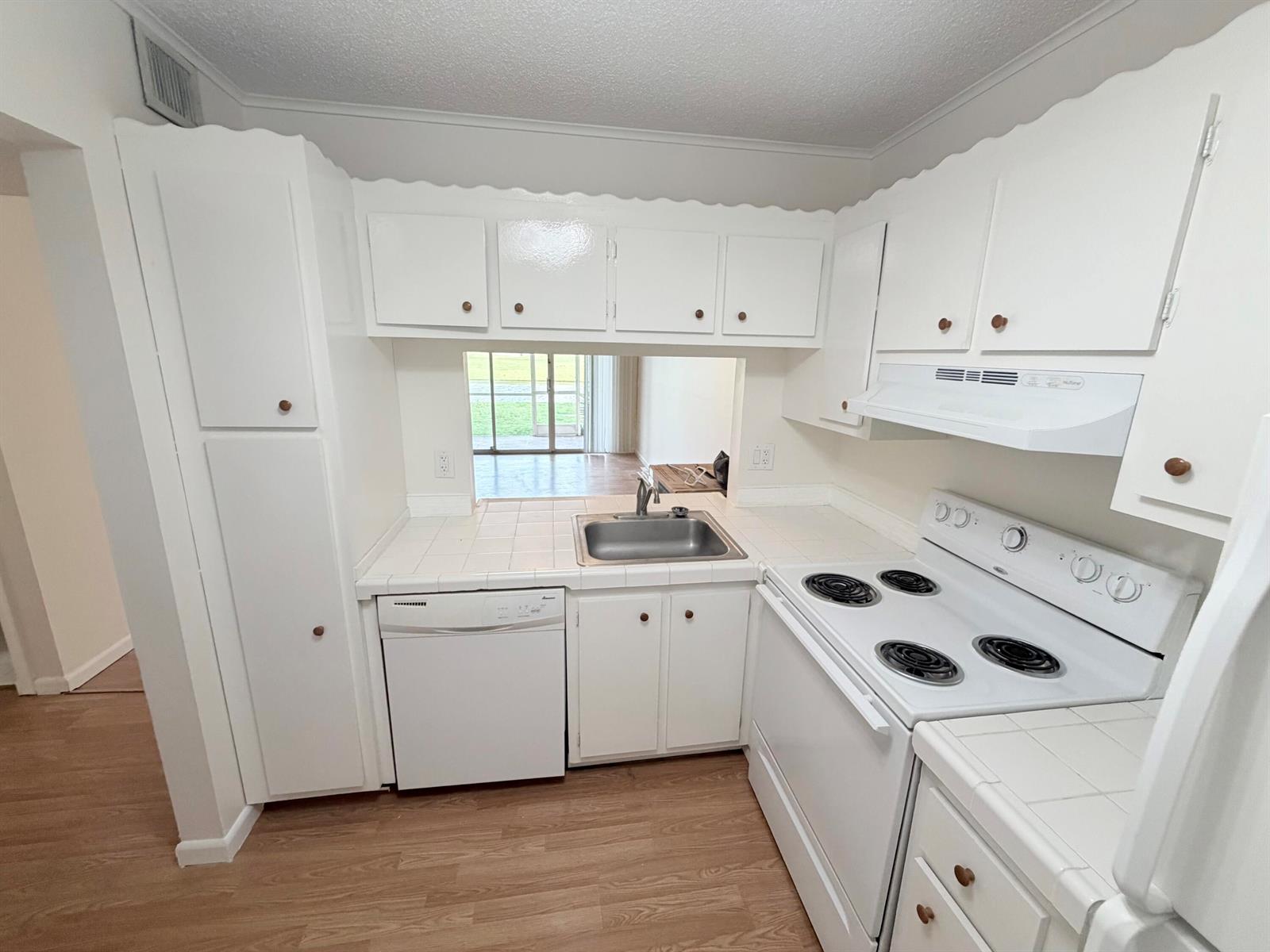 A kitchen features white cabinets, white appliances, tile countertops, and a pass-through window — 9230 Lagoon Place # 110, Davie FL 33324, DAVIE, FL