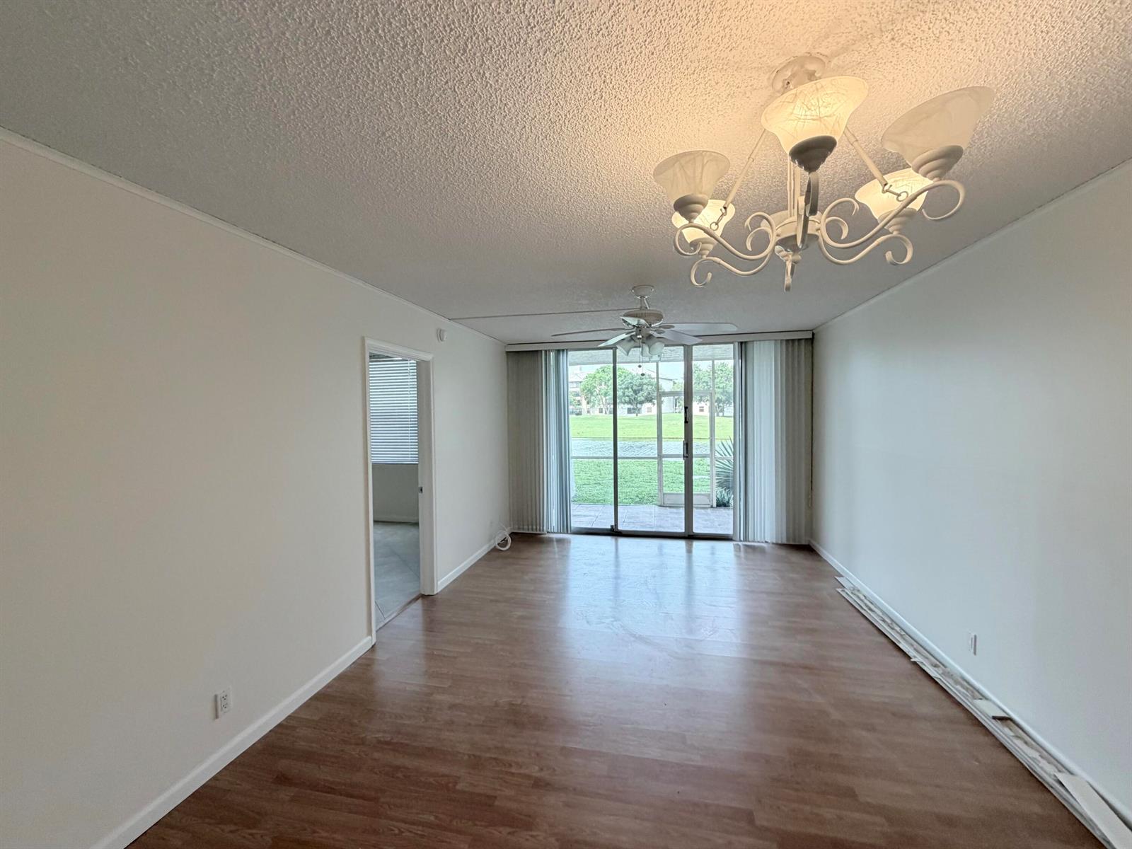 An empty living room with wood-look flooring, a white chandelier, and sliding glass patio doors — 9230 Lagoon Place # 110, Davie FL 33324, DAVIE, FL