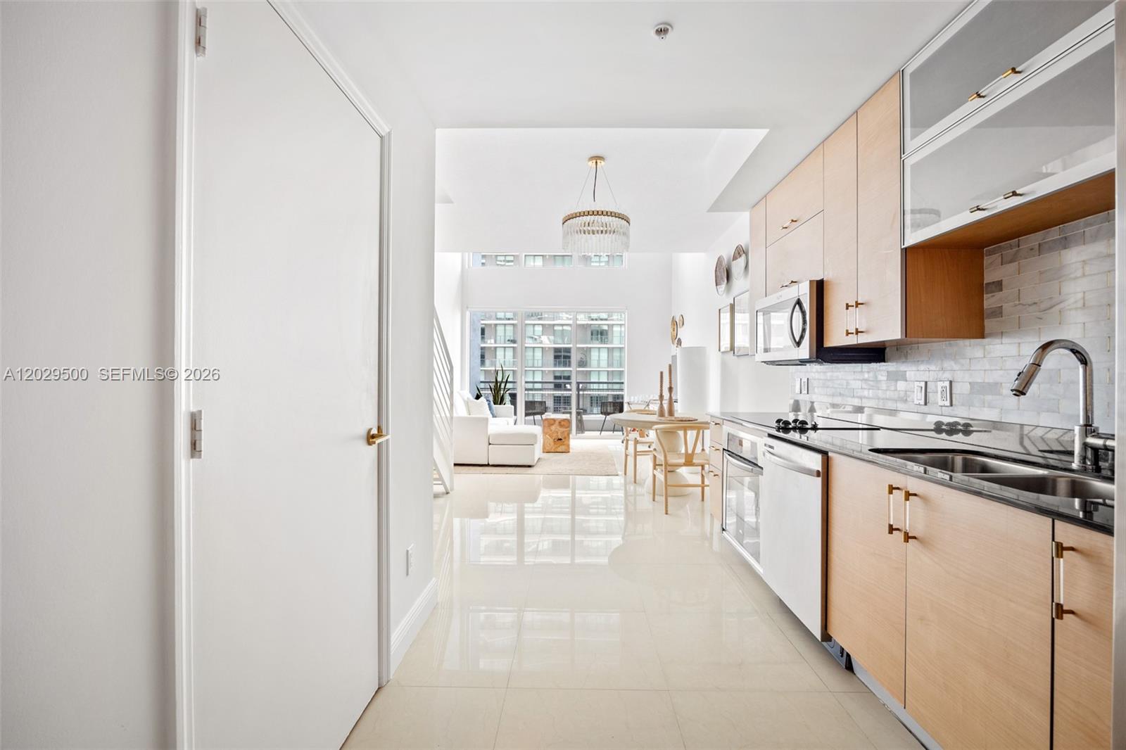 A modern kitchen with light wood cabinets and white tile floors opens into a living area — 60 SW 13th St # 3414, Miami FL 33130, MIAMI, FL