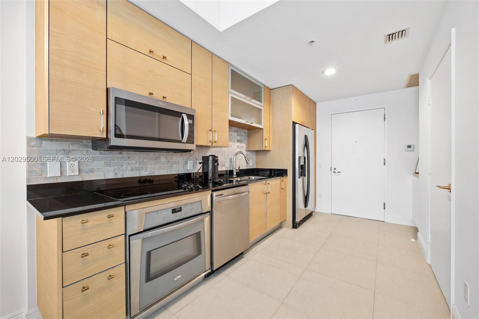 A modern kitchen features light wood cabinets, black countertops, and stainless steel appliances — 60 SW 13th St # 3414, Miami FL 33130, MIAMI, FL