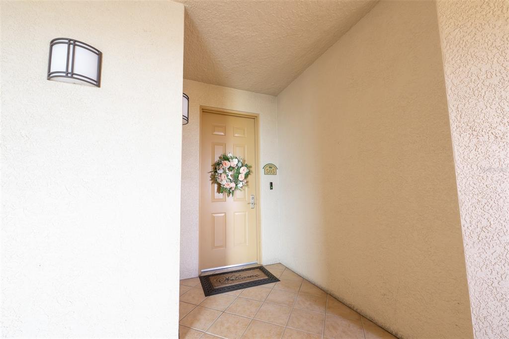 A beige front door with a floral wreath is set within a tiled entryway — 3414 HANCOCK BRIDGE PARKWAY UNIT 505, NORTH FORT MYERS, FL