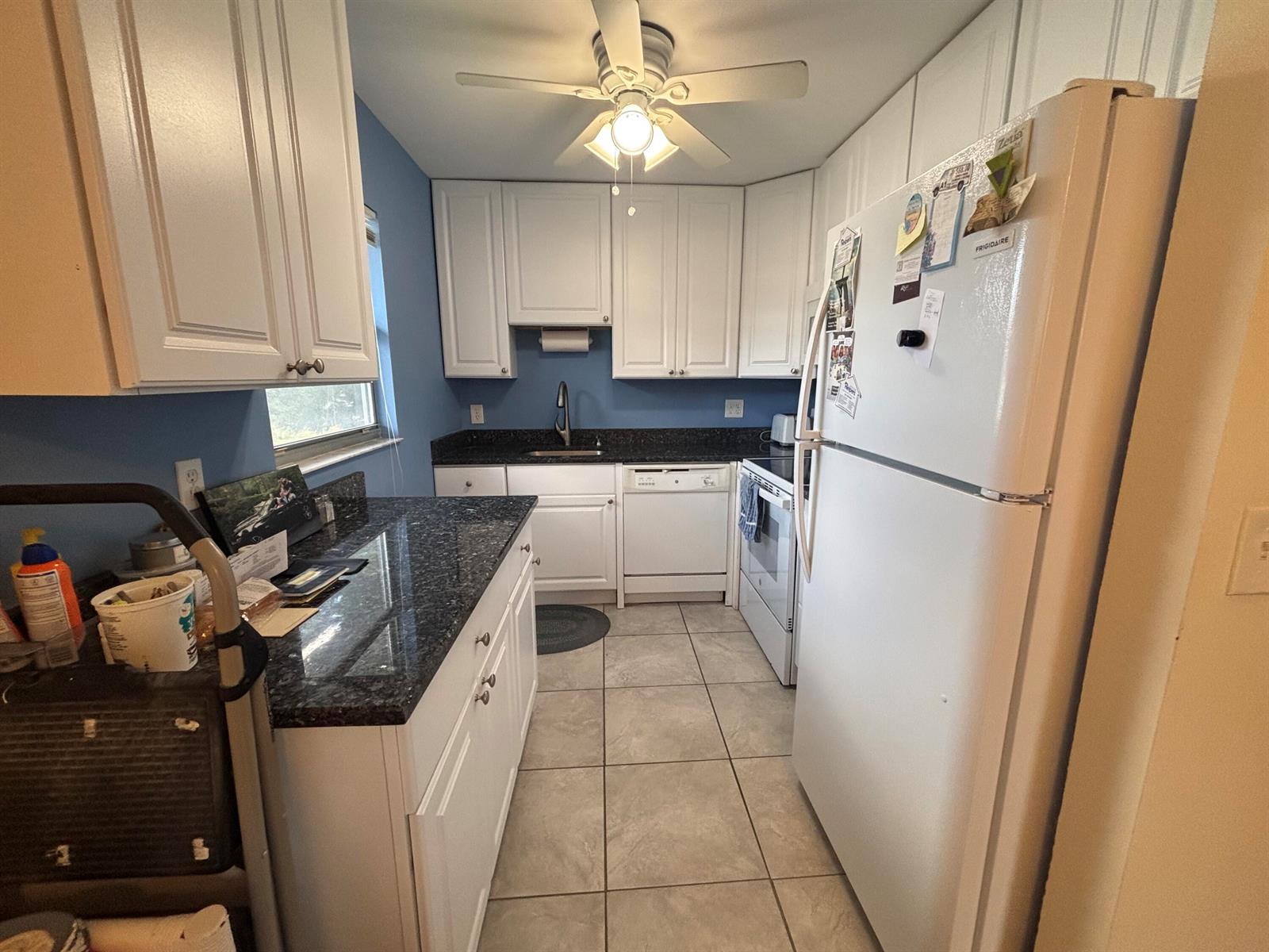 A kitchen features white cabinets, dark granite countertops, stainless steel appliances, and tile flooring — 596 Saxony M, Delray Beach FL 33446, DELRAY BEACH, FL