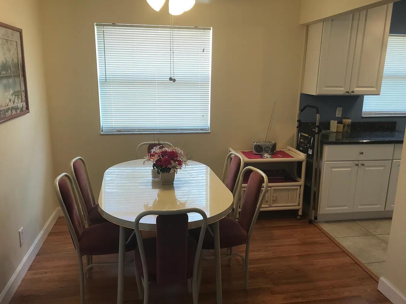 A dining area features a white oval table, four chairs, and a small serving cart — 596 Saxony M, Delray Beach FL 33446, DELRAY BEACH, FL