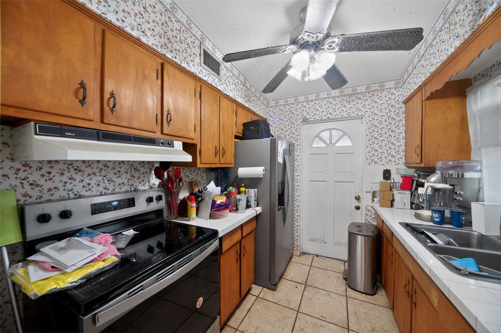 A kitchen features wood cabinets, floral wallpaper, a ceiling fan, and a stainless steel refrigerator — 2615 PEEL AVENUE, ORLANDO, FL