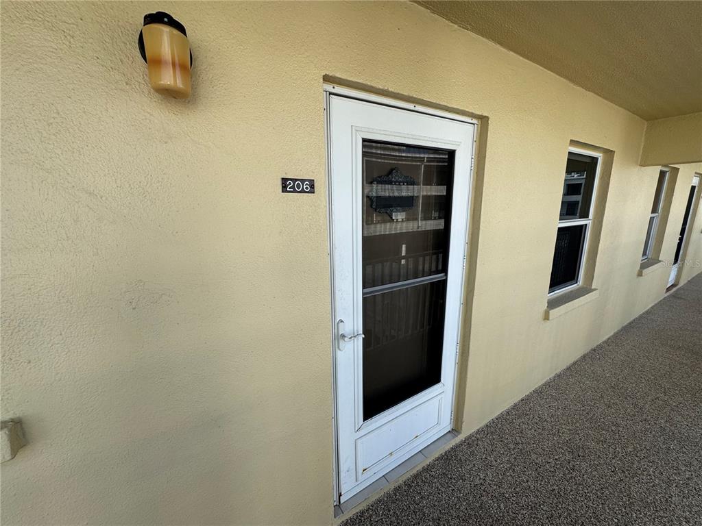 An exterior view of a building hallway showing unit 206 with a white storm door — 1400 TARPON CENTER DRIVE UNIT 206, VENICE, FL