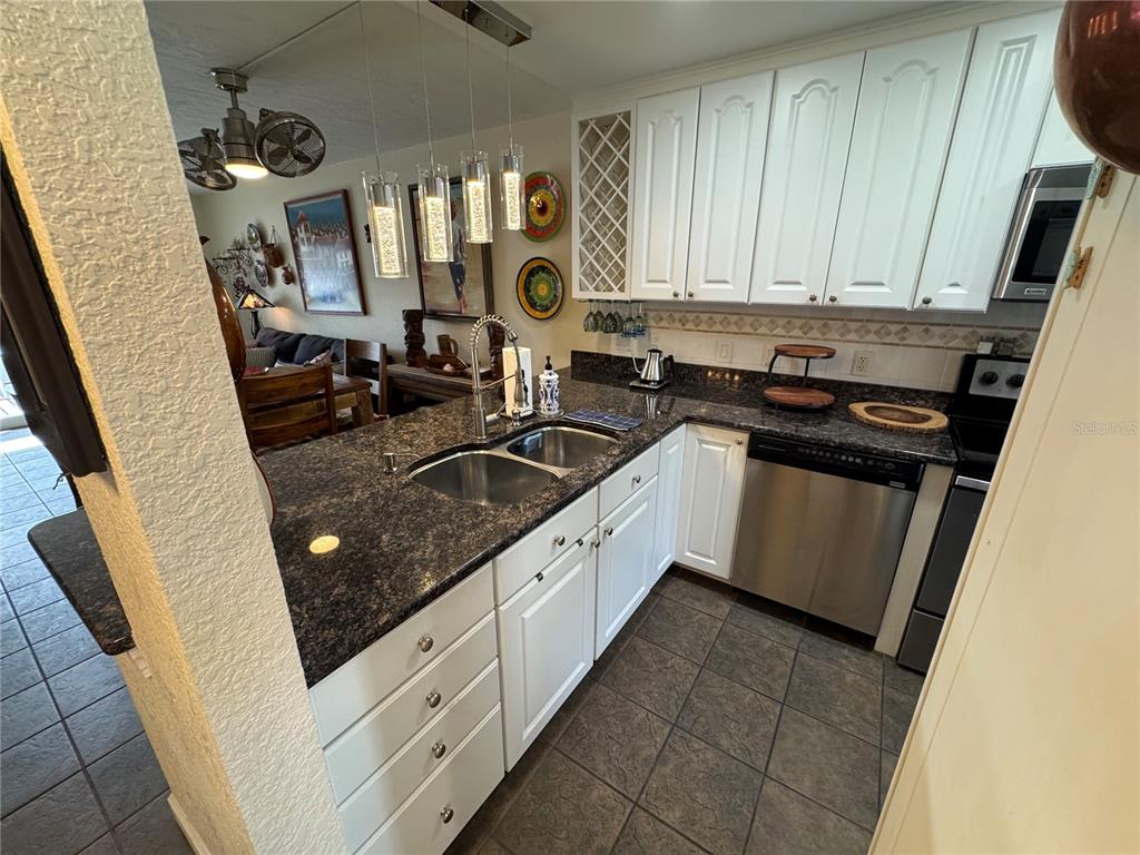 A kitchen features white cabinets, dark granite countertops, stainless steel appliances, and tile flooring — 1400 TARPON CENTER DRIVE UNIT 206, VENICE, FL