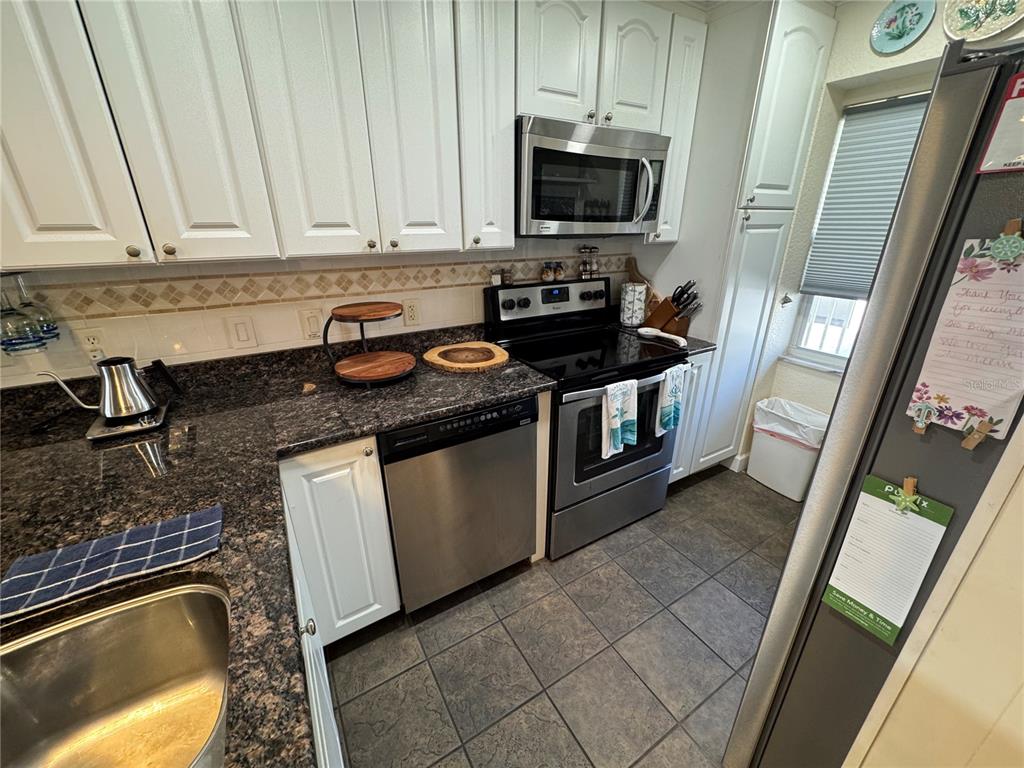 A kitchen with white cabinets, dark granite countertops, stainless steel appliances, and tiled flooring — 1400 TARPON CENTER DRIVE UNIT 206, VENICE, FL