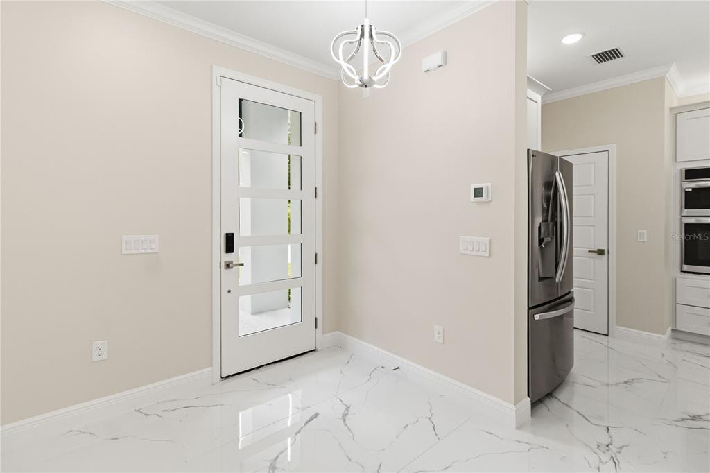 A bright entryway with white marble-look tile flooring, a glass-paneled door, and a modern chandelier — 2006 WILLIAMS AVENUE, SANFORD, FL