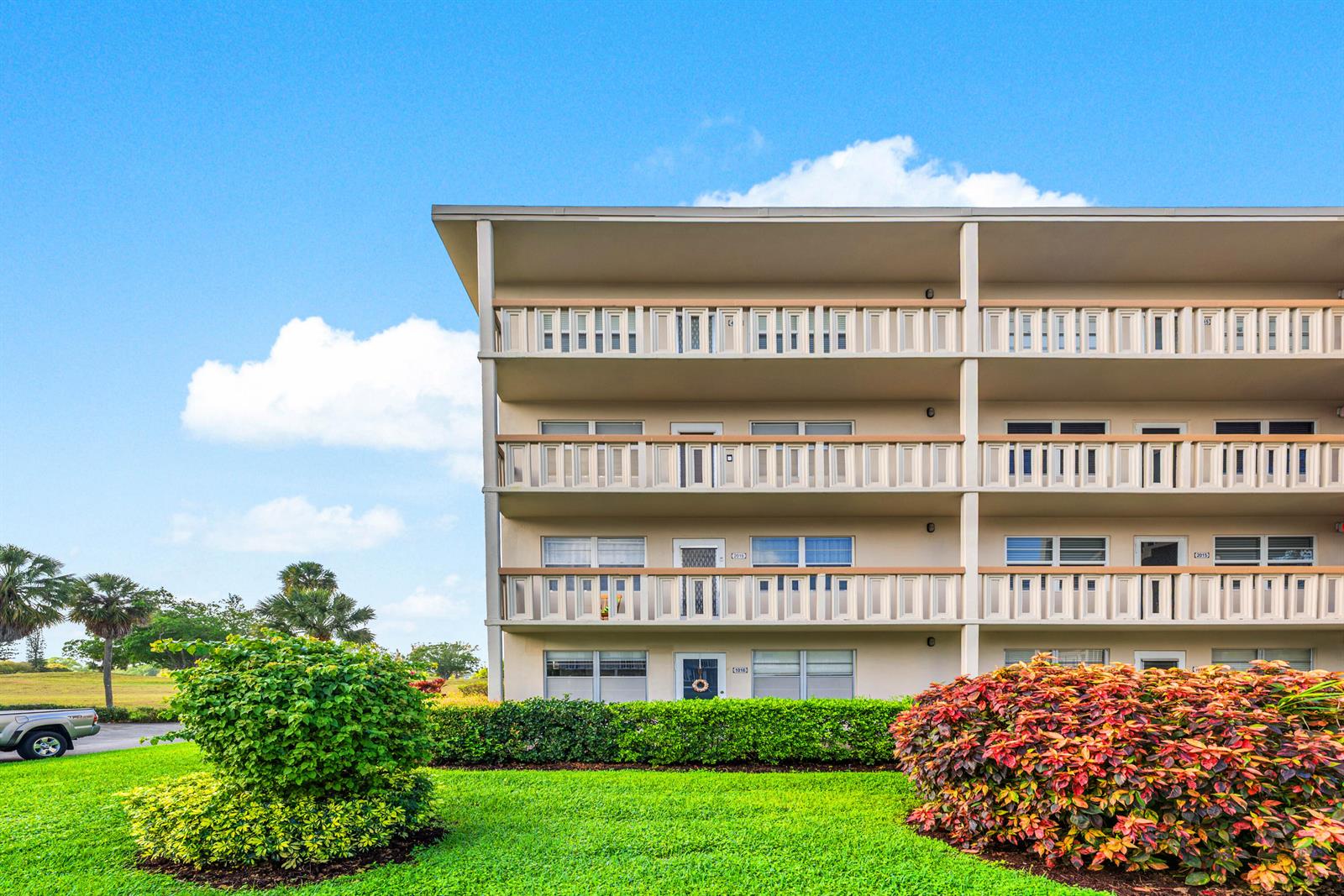A three-story apartment building features balconies with wooden railings and lush landscaping in front — 2016 Ventnor Crescent # G, Deerfield Beach FL 33442, DEERFIELD BEACH, FL