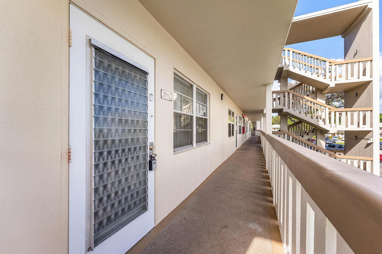 An exterior walkway leads past a door numbered 2016 toward a multi-story outdoor staircase — 2016 Ventnor Crescent # G, Deerfield Beach FL 33442, DEERFIELD BEACH, FL