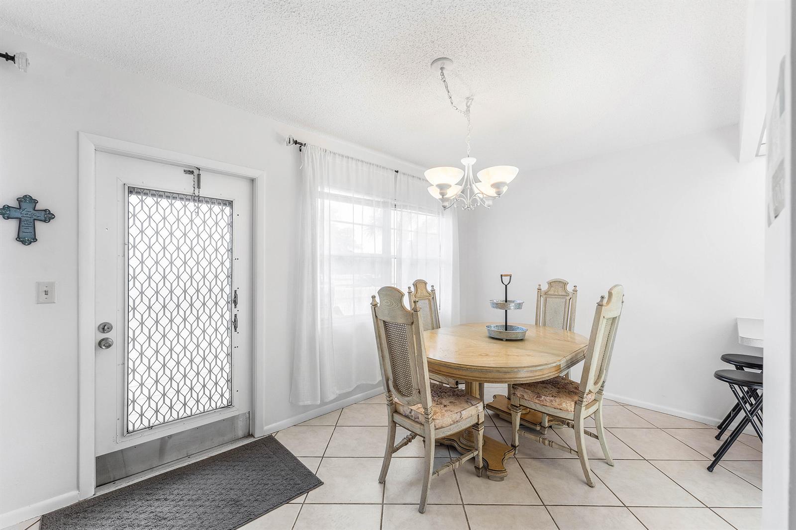 A dining area features a round wooden table, four chairs, a chandelier, and a door — 2016 Ventnor Crescent # G, Deerfield Beach FL 33442, DEERFIELD BEACH, FL
