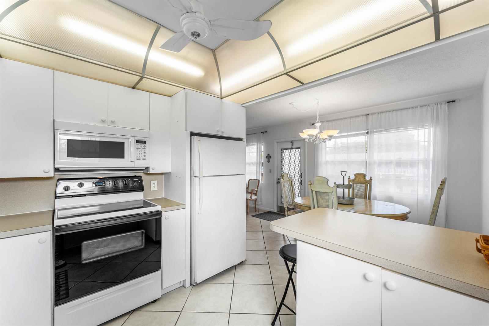A white kitchen with a stove, microwave, and refrigerator opens to a dining area — 2016 Ventnor Crescent # G, Deerfield Beach FL 33442, DEERFIELD BEACH, FL