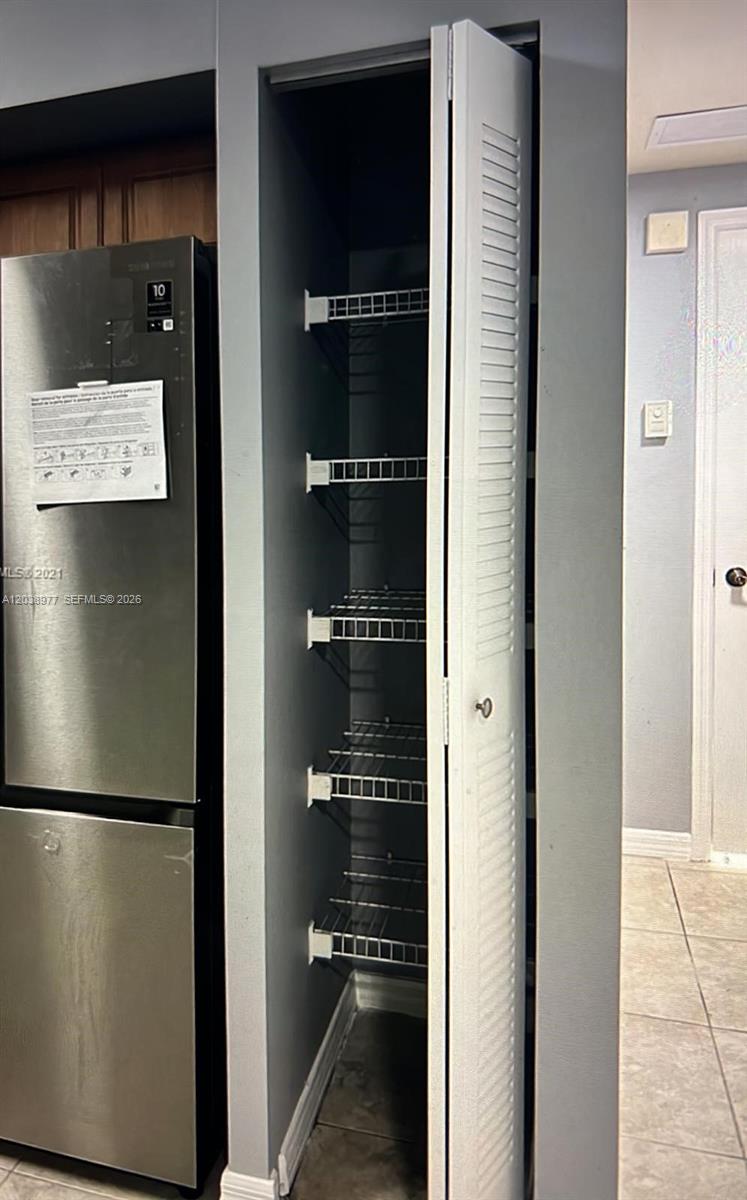 A tall, narrow pantry with white louvered doors and wire shelving sits beside a refrigerator — 115 SW 42nd Ave # 206, Miami FL 33134, MIAMI, FL
