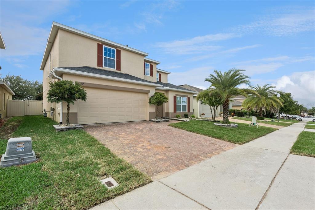 A two-story suburban house with a tan stucco exterior, a brick driveway, and palm trees — 2227 NAPONE LANE, MINNEOLA, FL