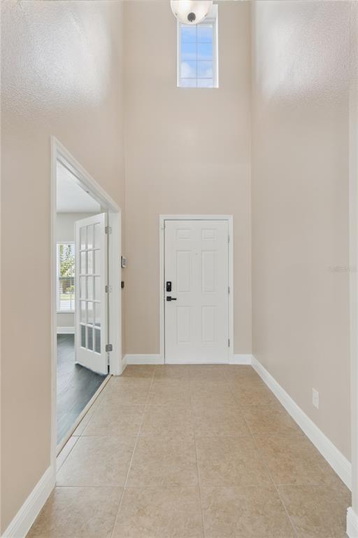 A high-ceilinged entryway features beige tile flooring, a white front door, and a French door — 2227 NAPONE LANE, MINNEOLA, FL
