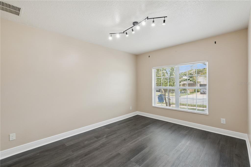 An empty bedroom features beige walls, dark wood-look flooring, and a modern track light fixture — 2227 NAPONE LANE, MINNEOLA, FL