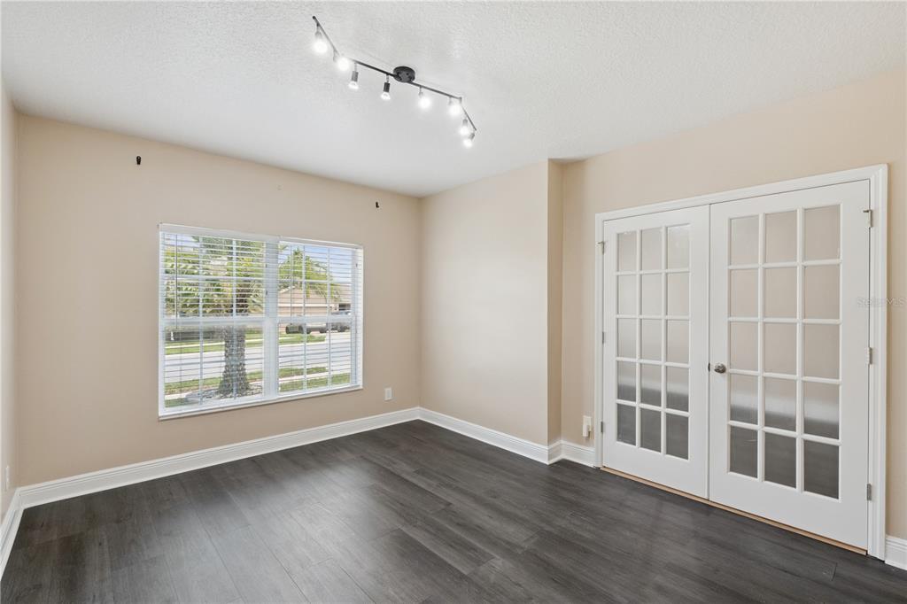 An empty room with dark wood-look flooring, beige walls, a track light, and French doors — 2227 NAPONE LANE, MINNEOLA, FL
