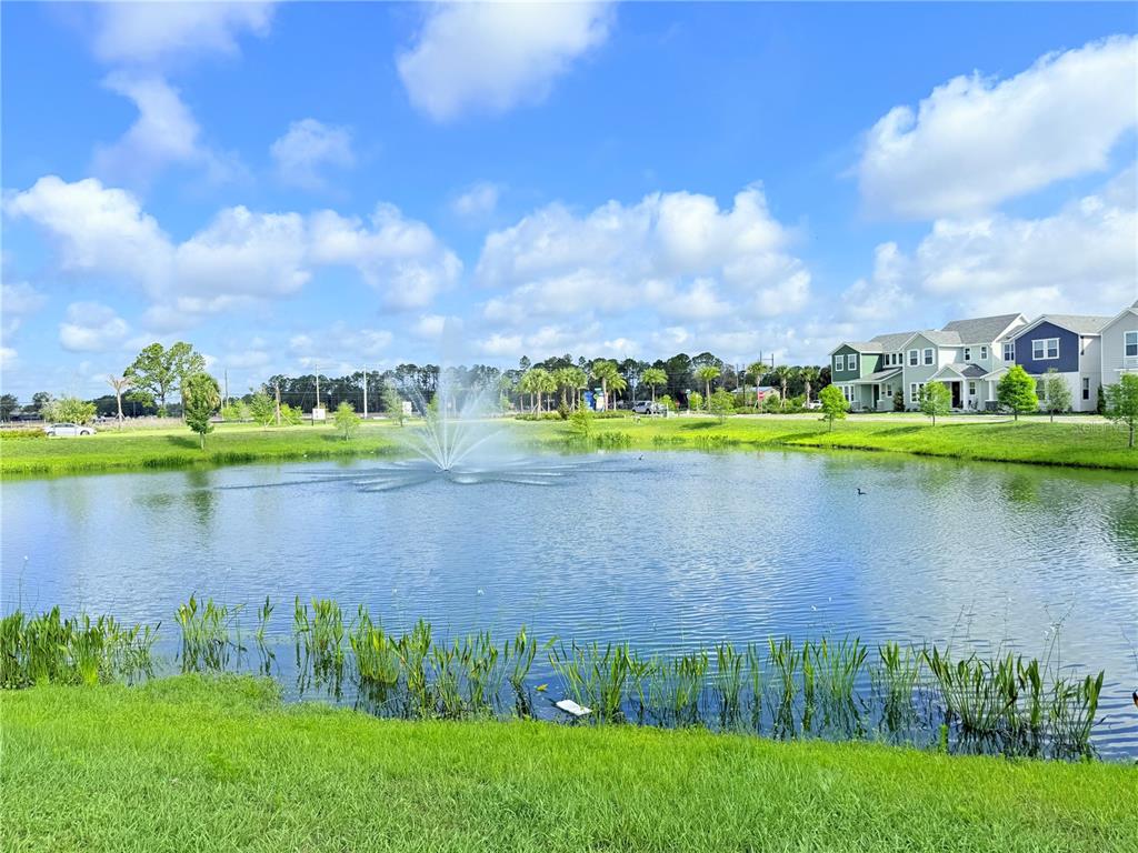 A pond with a fountain sits in front of suburban houses under a blue sky — 237 STATION LANE, DEBARY, FL