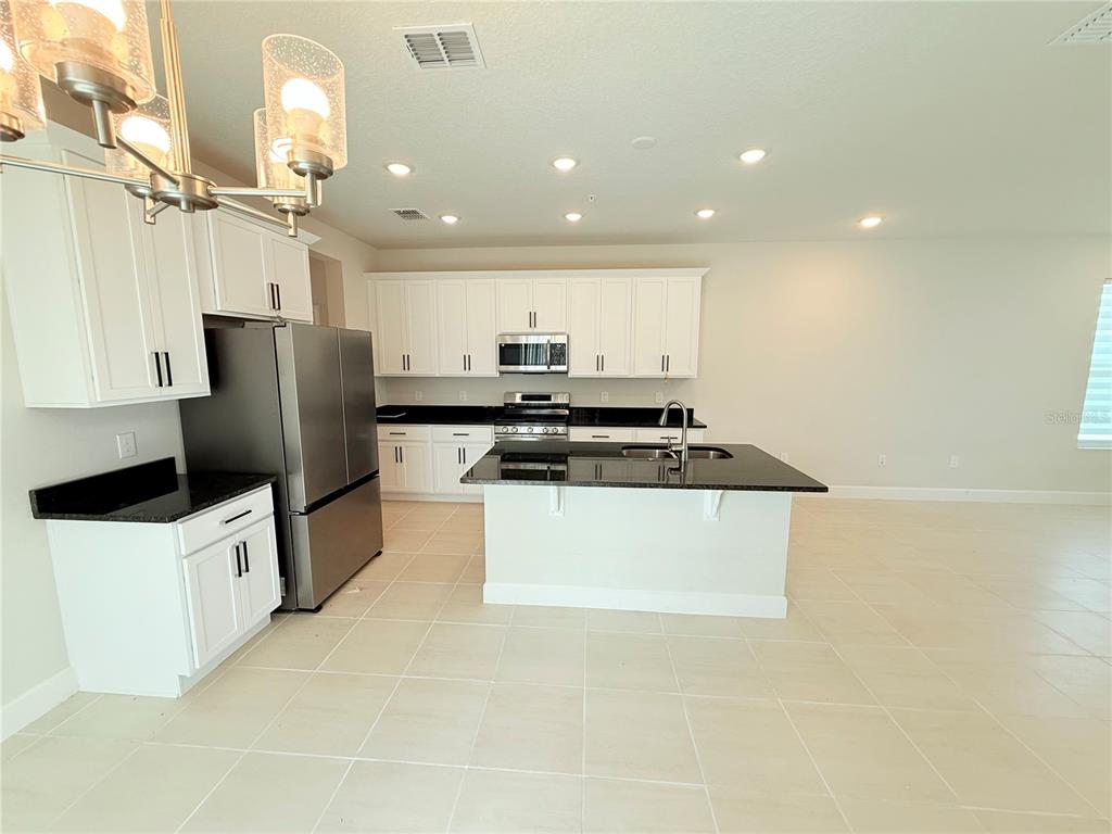 A kitchen features white cabinets, stainless steel appliances, a black countertop island, and tile flooring — 237 STATION LANE, DEBARY, FL