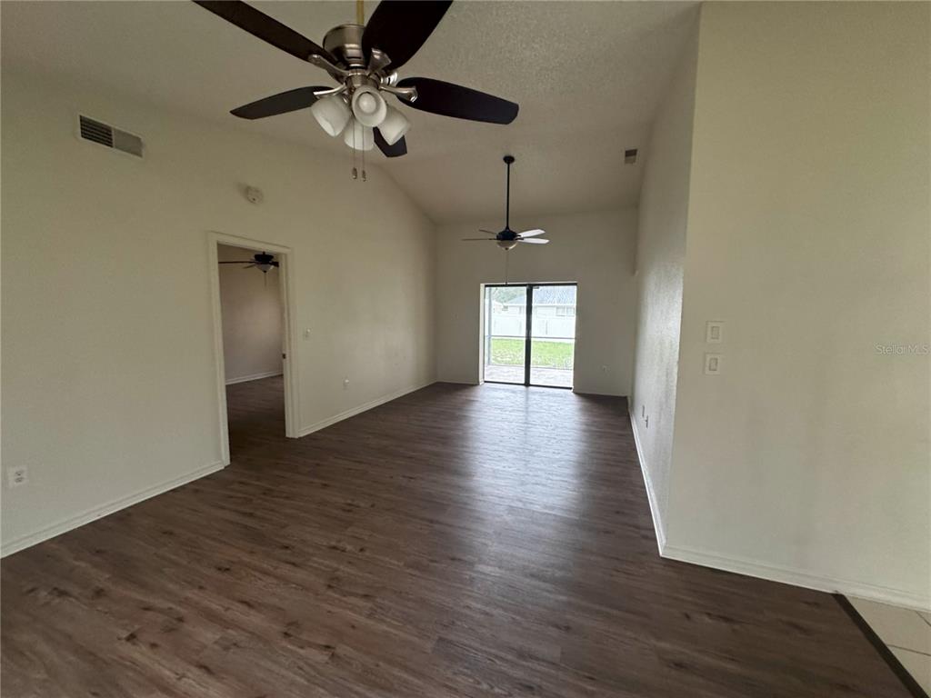 An empty living room features wood-look flooring, vaulted ceilings, two ceiling fans, and sliding doors — 2378 COMERWOOD DRIVE, SPRING HILL, FL