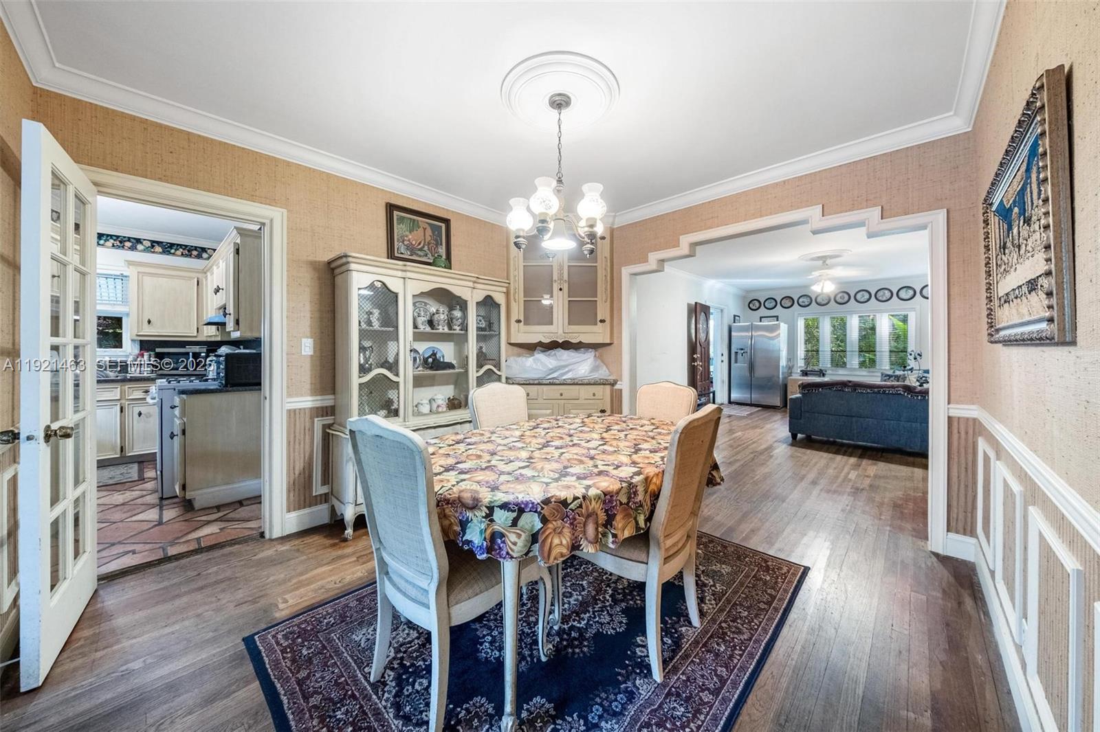 A dining room with a floral tablecloth, hutch, and wood flooring opens to a kitchen — 37 NE 44th St, Miami FL 33137, MIAMI, FL