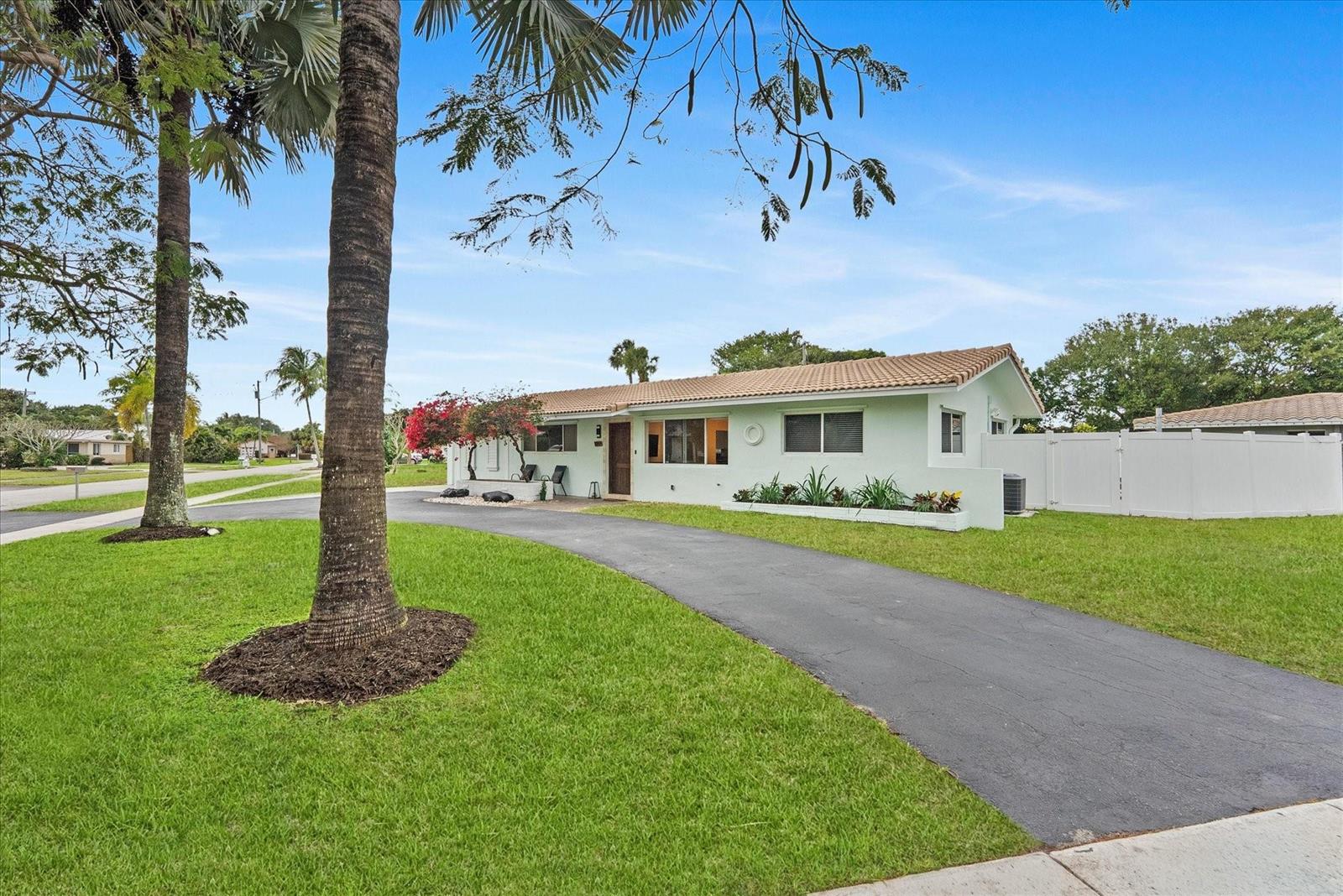 A light green single-story house features a curved asphalt driveway and a white privacy fence — 1257 NW 5th Street, Boca Raton FL 33486, BOCA RATON, FL