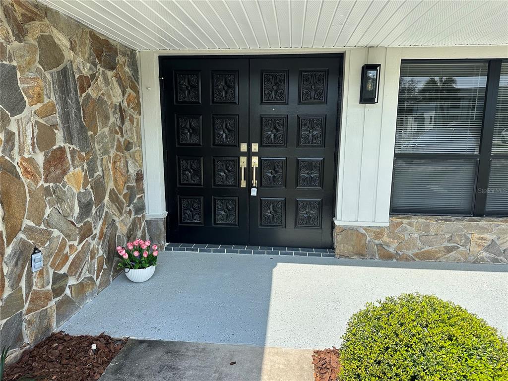 A black double front door with decorative panels sits beside a stone-clad exterior wall — 5012 S DEEP WATER POINT, HOMOSASSA, FL