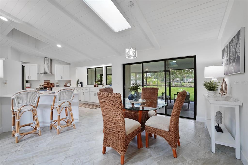 A bright, open-concept kitchen and dining area features white cabinetry, wicker chairs, and sliding doors — 5012 S DEEP WATER POINT, HOMOSASSA, FL