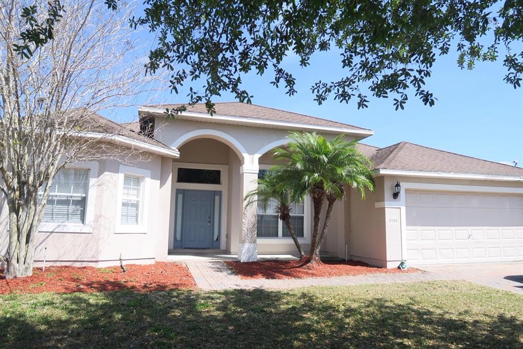 A single-story house with a beige stucco exterior, a blue front door, and a palm tree — 2906 SWEETSPIRE CIRCLE, KISSIMMEE, FL
