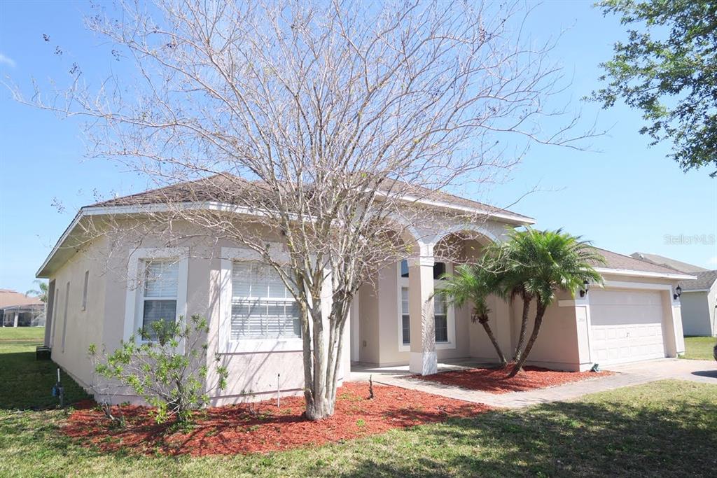 A single-story beige house with a two-car garage and a large tree in front — 2906 SWEETSPIRE CIRCLE, KISSIMMEE, FL