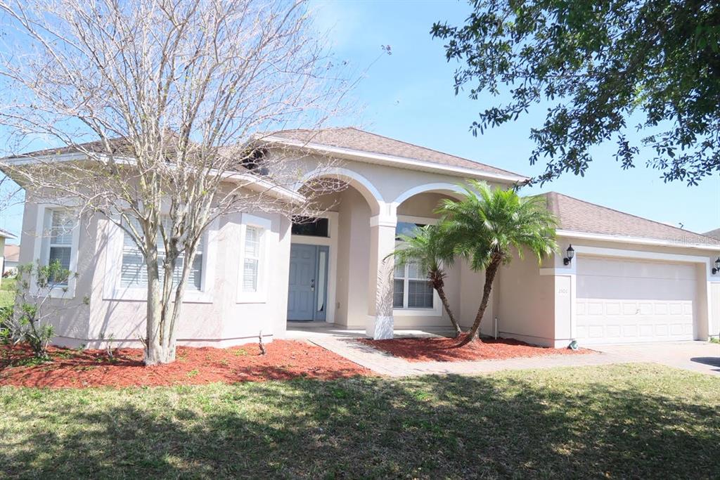 A single-story beige house with a two-car garage, arched entryway, and a palm tree — 2906 SWEETSPIRE CIRCLE, KISSIMMEE, FL