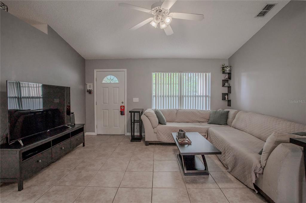 A living room features tile flooring, a sectional sofa, a television, and a ceiling fan — 1495 3RD STREET, ORANGE CITY, FL