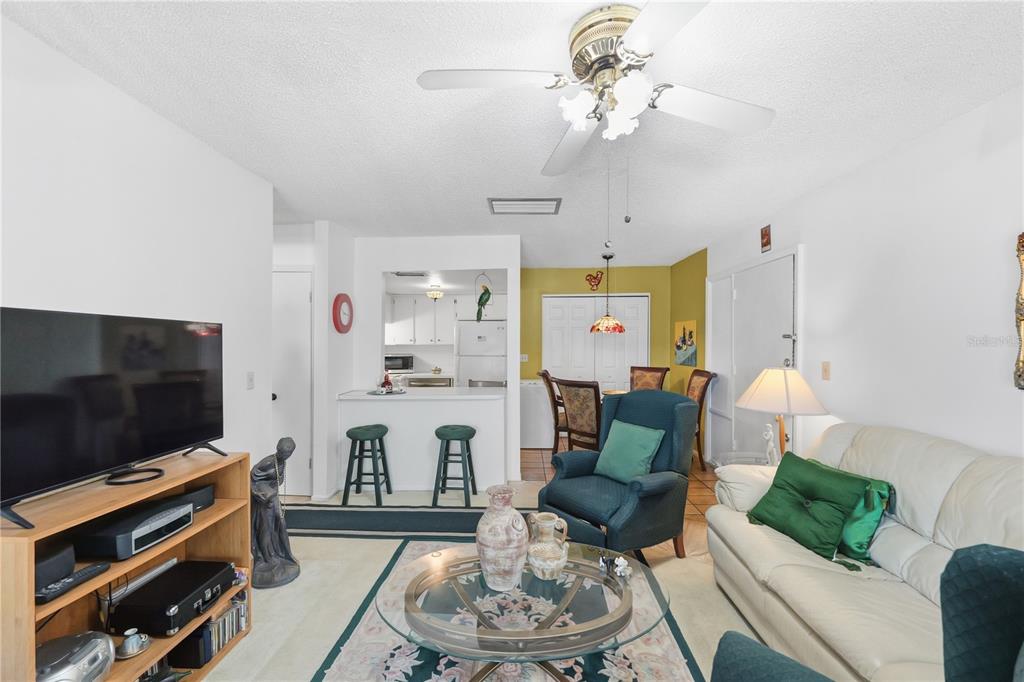 A living room with a white sofa, blue armchair, glass coffee table, and open kitchen — 3853 S LAKE DRIVE UNIT 165, TAMPA, FL