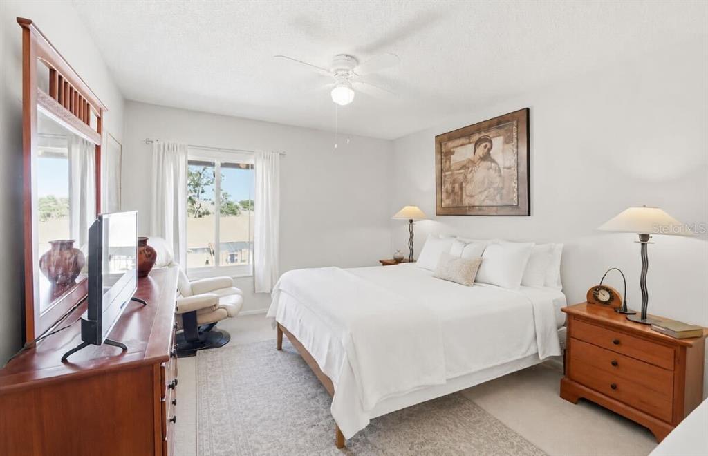 A bedroom features a white bed, a wooden dresser with a television, and a window — 3853 S LAKE DRIVE UNIT 165, TAMPA, FL