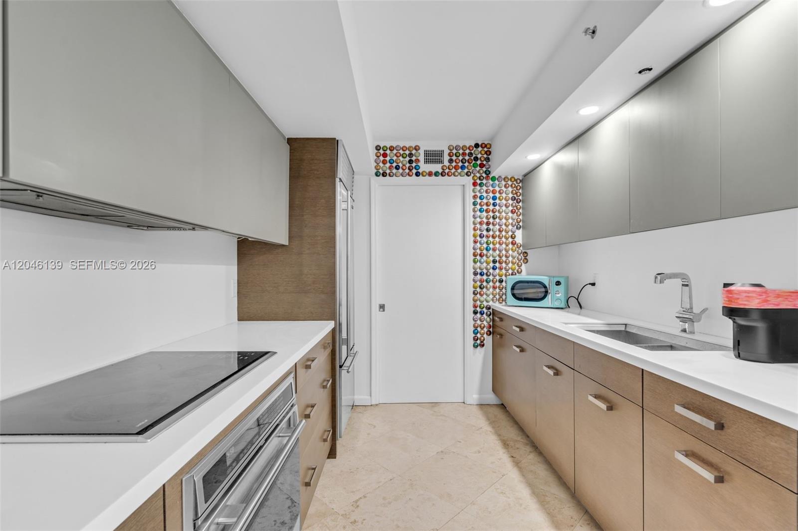 A galley kitchen features light wood cabinets, white countertops, and a wall decorated with colorful capsules — 6917 Collins Ave # 404, Miami Beach FL 33141, MIAMI BEACH, FL