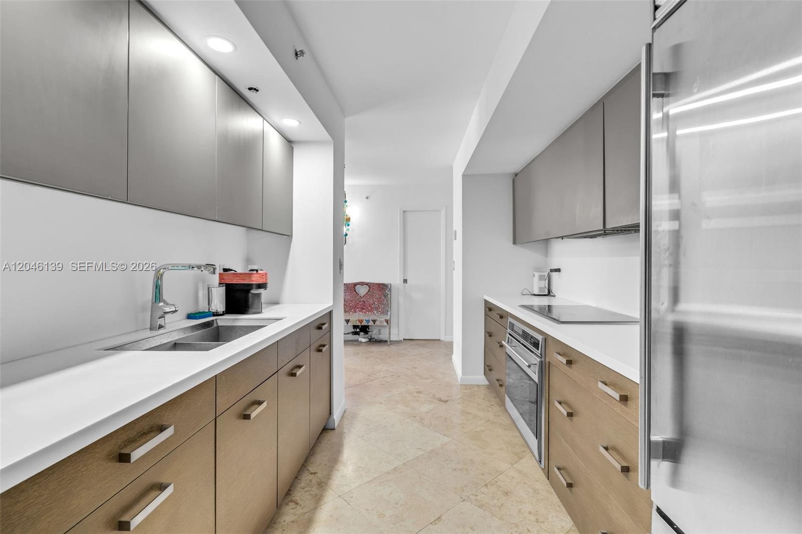 A galley kitchen features light wood cabinets, white countertops, and stainless steel appliances — 6917 Collins Ave # 404, Miami Beach FL 33141, MIAMI BEACH, FL