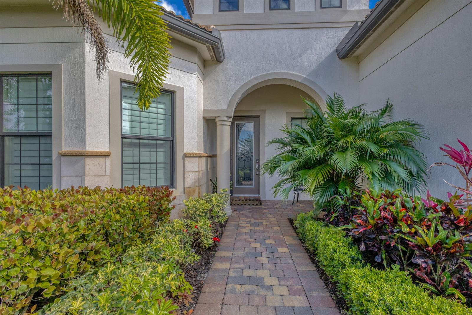 A paved walkway leads to the arched entryway of a house with light-colored stucco walls — 532 Sonoma Isles Circle, Jupiter FL 33478, JUPITER, FL
